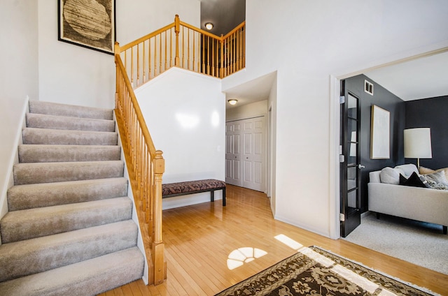 stairway with visible vents, a towering ceiling, hardwood / wood-style flooring, and baseboards