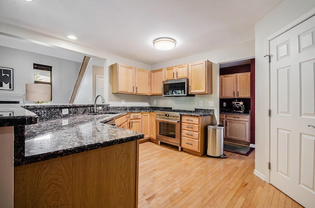 kitchen with light brown cabinetry, appliances with stainless steel finishes, a sink, light wood-type flooring, and a peninsula