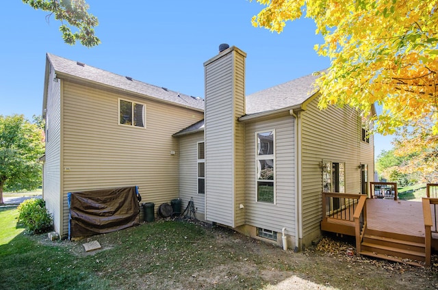 back of property featuring a chimney, a deck, a lawn, and roof with shingles