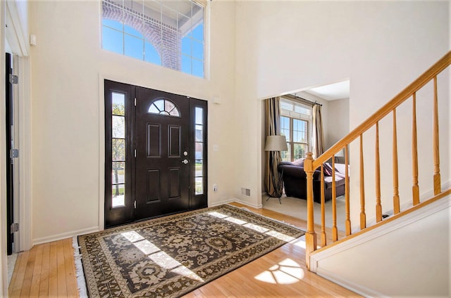 entryway featuring wood-type flooring, visible vents, a towering ceiling, stairway, and baseboards