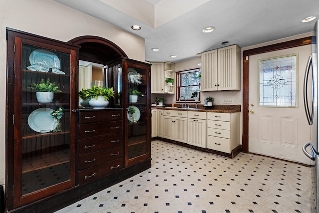 kitchen with dark countertops, cream cabinets, a sink, and recessed lighting