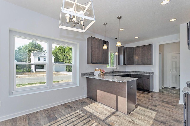 kitchen featuring light hardwood / wood-style flooring, sink, light stone countertops, kitchen peninsula, and dark brown cabinetry