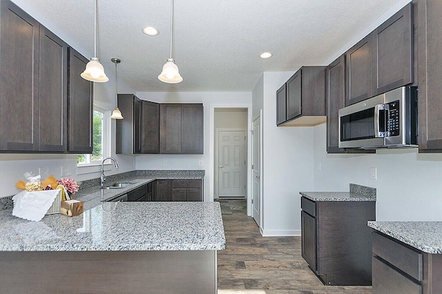 kitchen with dark wood-type flooring, dark brown cabinetry, light stone countertops, pendant lighting, and sink