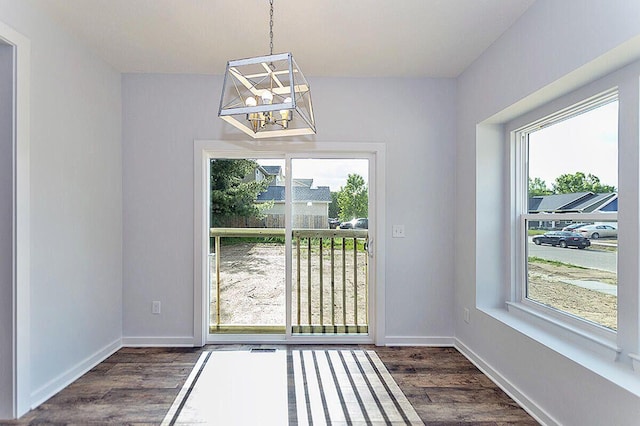 unfurnished dining area featuring a notable chandelier, plenty of natural light, and dark wood-type flooring