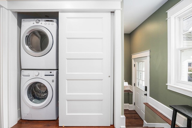 laundry room featuring plenty of natural light, dark wood-type flooring, and stacked washing maching and dryer