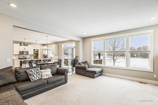 living area with a textured ceiling, baseboards, a notable chandelier, and light colored carpet