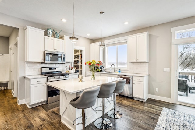 kitchen featuring appliances with stainless steel finishes, a center island, hanging light fixtures, light countertops, and white cabinetry