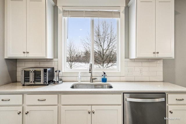 kitchen featuring tasteful backsplash, white cabinets, dishwasher, and a sink