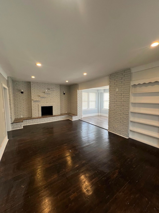 unfurnished living room featuring a brick fireplace, wood-type flooring, and brick wall