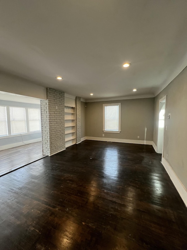 unfurnished living room with a healthy amount of sunlight, dark hardwood / wood-style flooring, and built in shelves