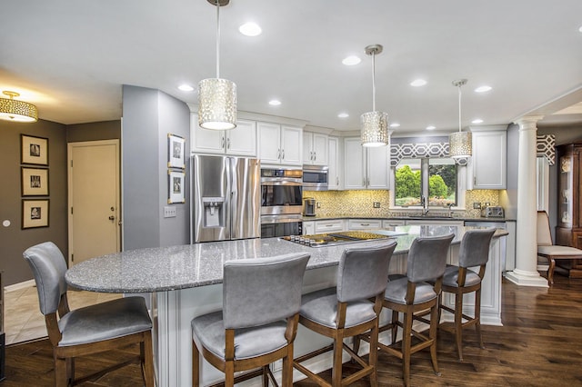 kitchen featuring pendant lighting, tasteful backsplash, appliances with stainless steel finishes, white cabinetry, and ornate columns