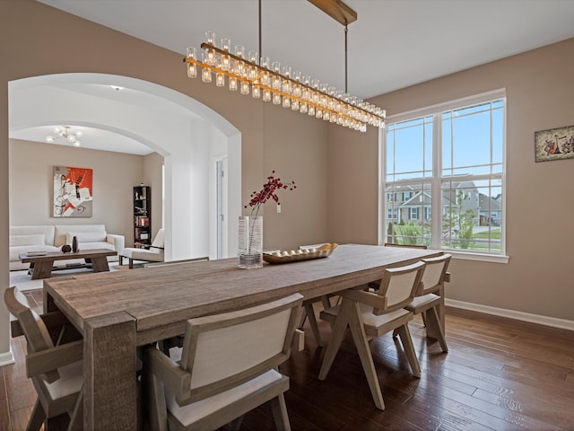 dining space with arched walkways, dark wood-style flooring, and baseboards