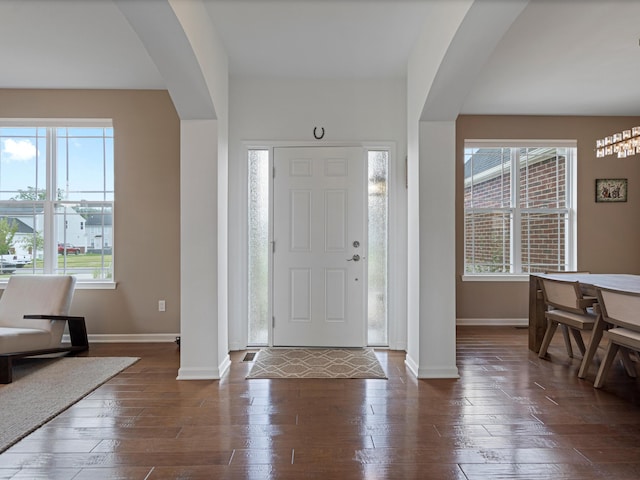 foyer entrance featuring arched walkways, dark wood-style floors, and baseboards