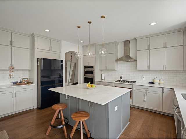 kitchen with dark wood finished floors, a kitchen island, appliances with stainless steel finishes, wall chimney range hood, and pendant lighting