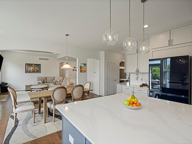 kitchen with decorative light fixtures, tasteful backsplash, visible vents, refrigerator with glass door, and light stone countertops