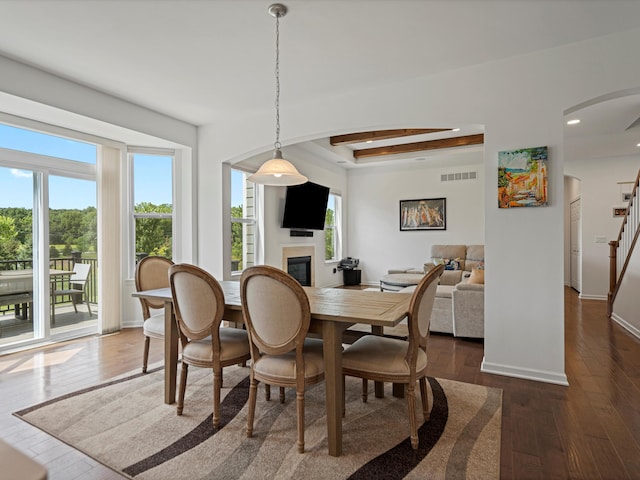 dining space featuring arched walkways, a glass covered fireplace, visible vents, stairway, and dark wood finished floors