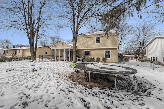 snow covered back of property with a trampoline, a sunroom, and fence