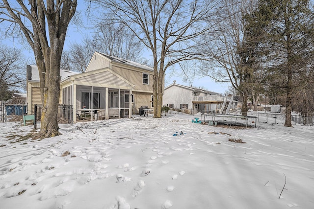 snow covered house featuring a chimney, fence, and a sunroom