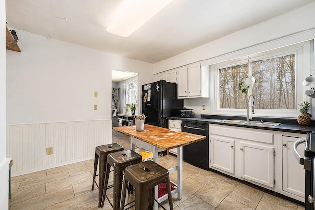 kitchen featuring dark countertops, wainscoting, a sink, white cabinetry, and black appliances