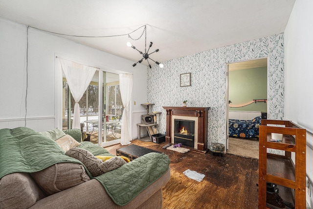 living room with a warm lit fireplace, a chandelier, wallpapered walls, and wood finished floors