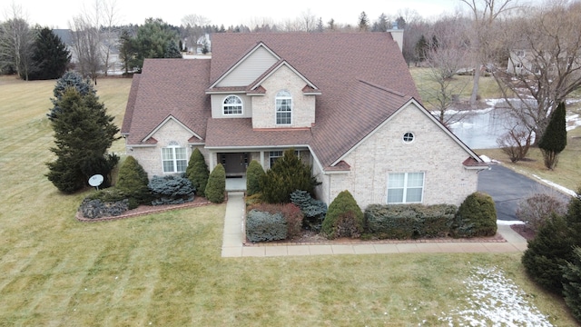 traditional home with roof with shingles, brick siding, a chimney, and a front yard
