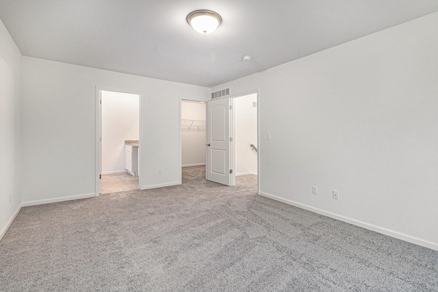 unfurnished bedroom featuring a walk in closet, a closet, visible vents, light carpet, and baseboards