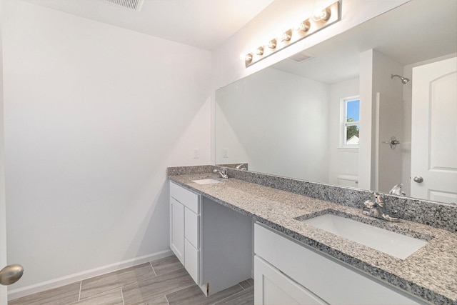 bathroom featuring double vanity, a sink, toilet, and baseboards