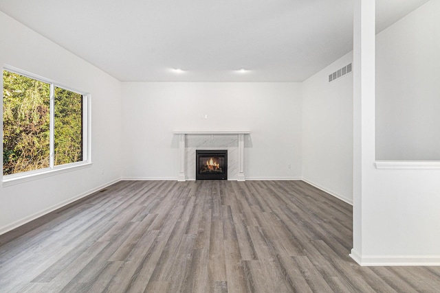 unfurnished living room with baseboards, a high end fireplace, visible vents, and light wood-style floors