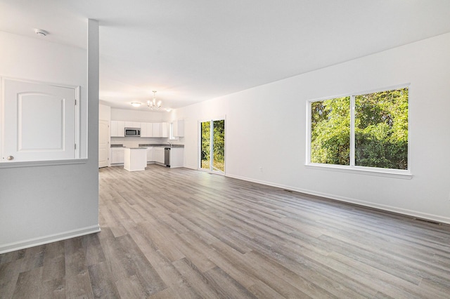 unfurnished living room featuring light wood-type flooring, visible vents, a notable chandelier, and baseboards