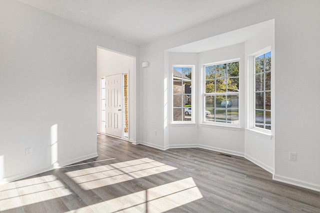 empty room featuring dark wood-style floors, visible vents, and baseboards