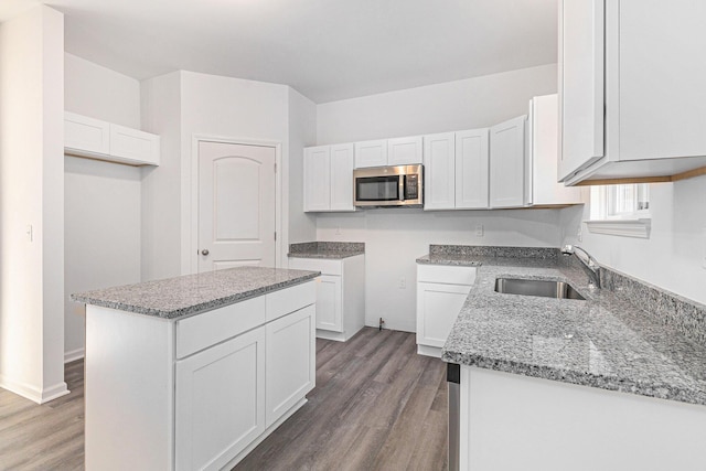 kitchen featuring a center island, stainless steel microwave, white cabinets, a sink, and light stone countertops