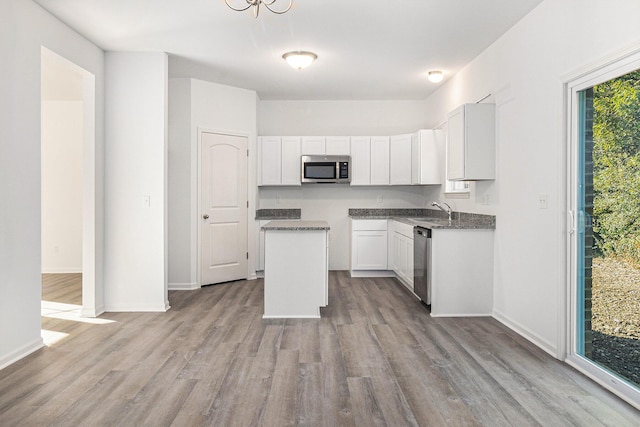 kitchen with light wood finished floors, white cabinets, appliances with stainless steel finishes, a center island, and a sink