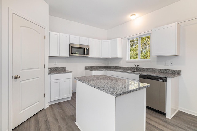 kitchen with a sink, a kitchen island, white cabinetry, appliances with stainless steel finishes, and dark wood-style floors