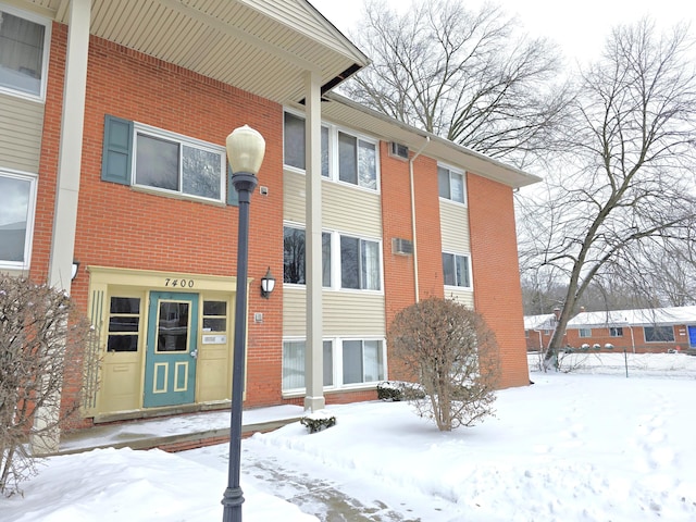 snow covered rear of property featuring brick siding