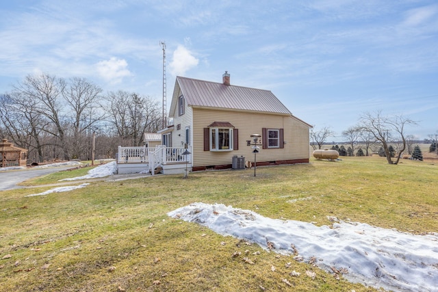 exterior space with a deck, metal roof, cooling unit, a lawn, and a chimney