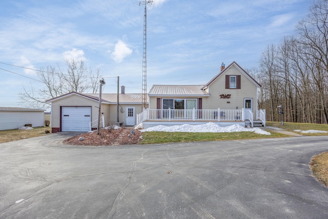 view of front facade with driveway, a chimney, metal roof, an attached garage, and a porch