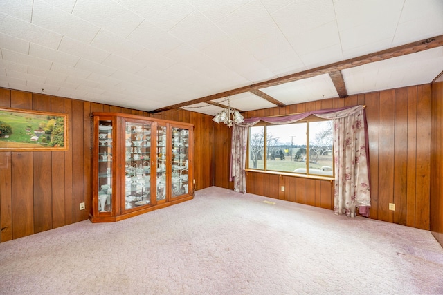 carpeted spare room featuring wood walls, beam ceiling, and an inviting chandelier