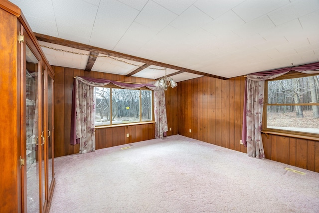 carpeted spare room featuring a chandelier, beamed ceiling, and wooden walls