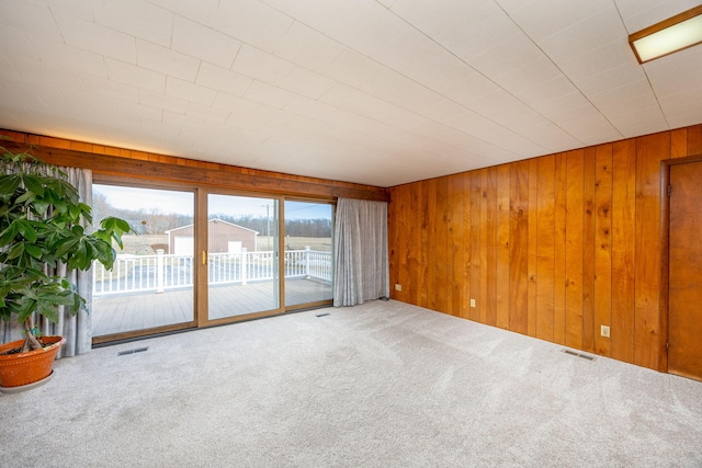 unfurnished room with carpet, visible vents, and wooden walls