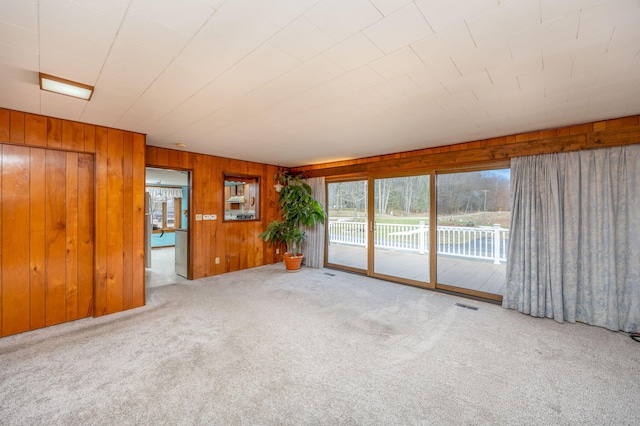 carpeted spare room with visible vents and wooden walls