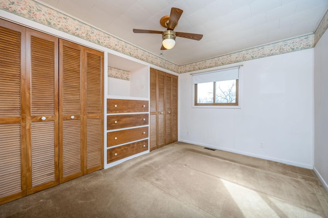 unfurnished bedroom with carpet, two closets, visible vents, ceiling fan, and baseboards