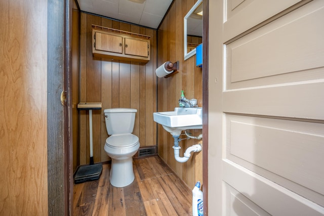 bathroom with toilet, wooden walls, visible vents, and wood finished floors