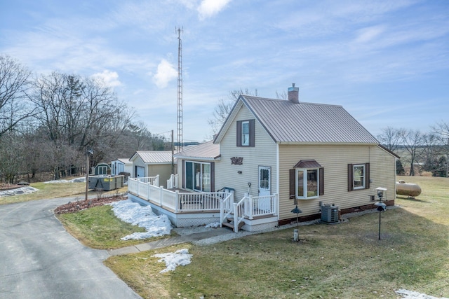 view of front facade with a deck, metal roof, a chimney, and a front yard