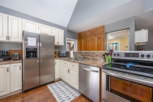 kitchen featuring tasteful backsplash, lofted ceiling, appliances with stainless steel finishes, a sink, and wood finished floors