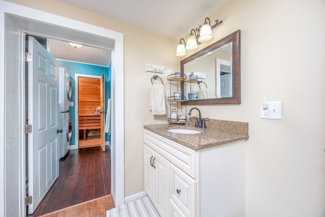 bathroom featuring stacked washer / dryer, wood finished floors, vanity, and baseboards