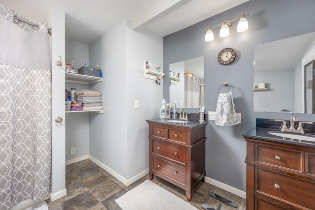 full bath with stone finish flooring, baseboards, two vanities, and a sink