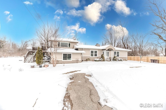 snow covered property featuring a chimney, stairs, and fence