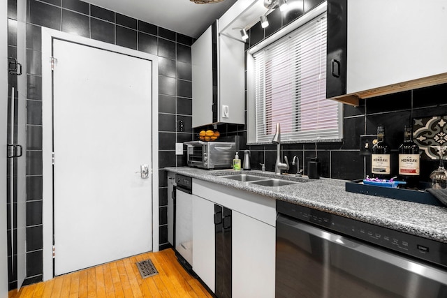 kitchen with a sink, visible vents, white cabinetry, stainless steel dishwasher, and tasteful backsplash