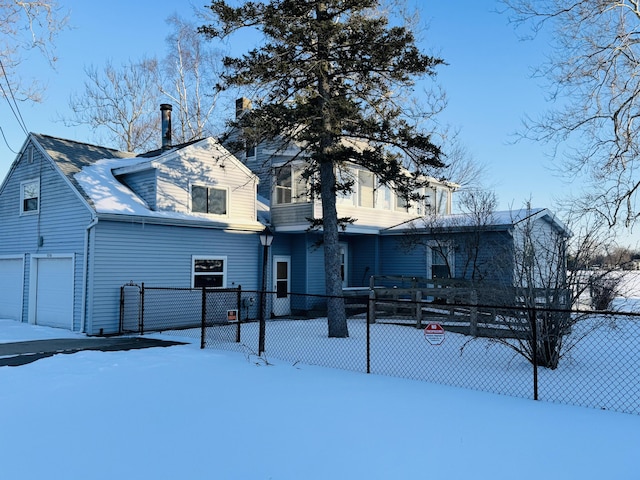 snow covered rear of property featuring a garage and fence