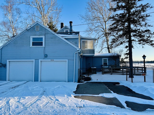 snow covered property with a garage, fence, and a chimney